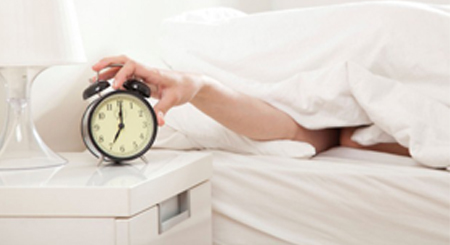 stock image of person turning off alarm clock while laying in bed